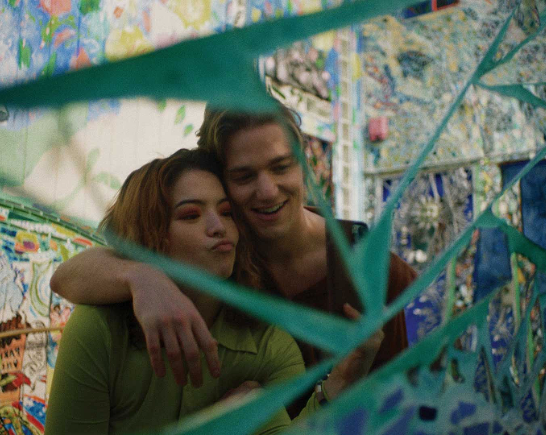 A female and male couple cuddle behind greenery