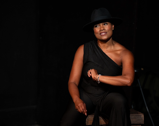 Beautiful Black woman in black hat in black open sleeve dress in play Earth, Wind and Car Fire
