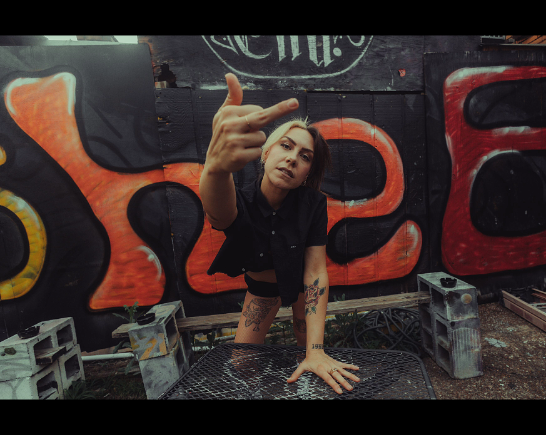 Singer performs on stage with Graffiti in the background as she leans into the camera with her middle finger raised