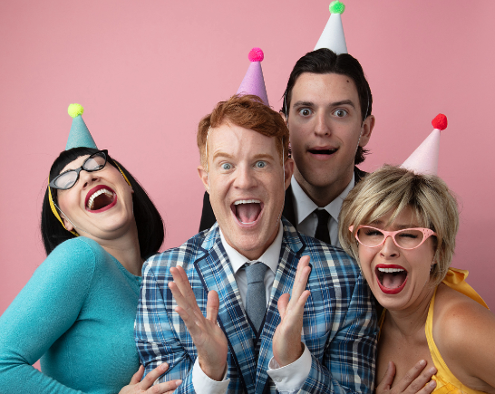 Two men and two women dressed in brightly colored clothes and party hats laughing
