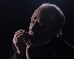 An man plays a french harp on stage in a post-civil war play