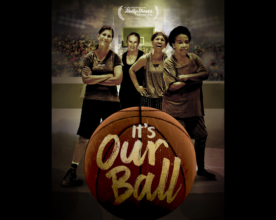 Four older women basketball players stand on a court behind a large basketball