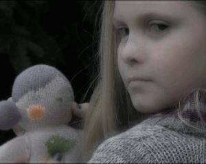 A young girl with long fair hair holds a knitted doll