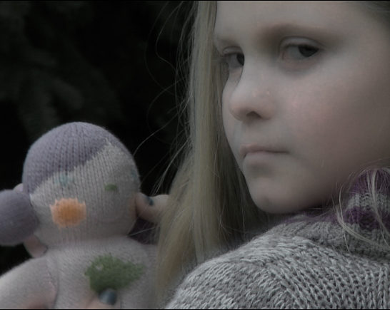 A young girl with long fair hair holds a knitted doll