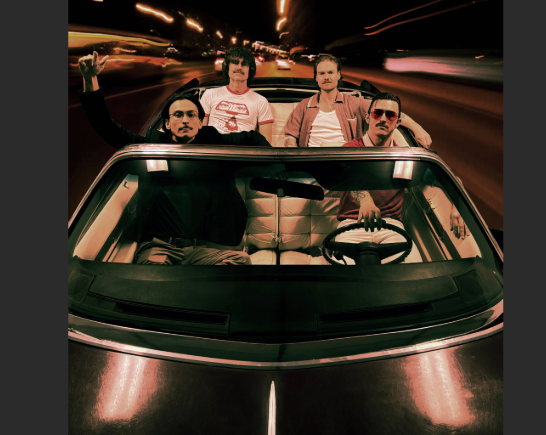 Four young men in the band Chief State drive through a tunnel in a convertible with the top down. The tone of the image is film noir...