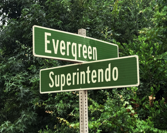 Green Street name sign with words Evergreen at the top and Superintendo below against a background of green foliage