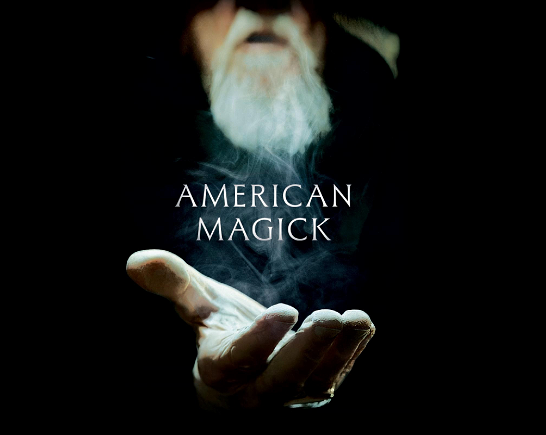 in a black background a white bearded face holds out a hand