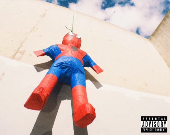 A spiderman pinata hangs against a beige stone wall above is a blue sky with white puffy clouds