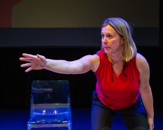 Actress Megan Dolan wears a red sleevelss shirt and black pants as she performs her show not the Right Mom