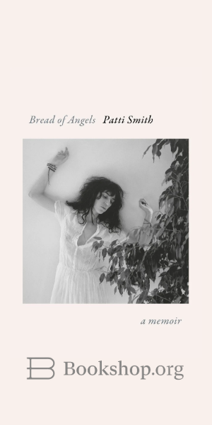 A black and white photo of a woman with long dark hair who wears a white dress her right arm raised in a fist as she looks toward a leafy plant. Book cover for Patti Smith Bread of Angels
