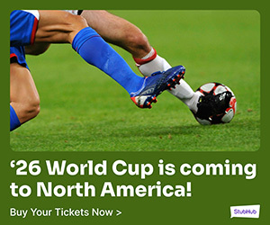 Two athletic legs wearing soccer socks and cleats reach across the frame to kick a soccer ball