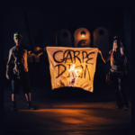 2 Skateboard punk rockers hold a burning sign between them with the words Carpe Diem spray painted on it