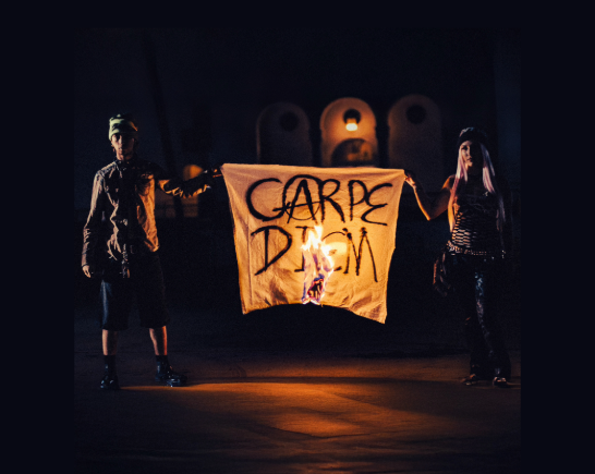 2 Skateboard punk rockers hold a burning sign between them with the words Carpe Diem spray painted on it