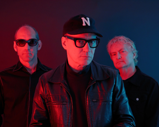 The three male members of the band Sour Ops stand together washed in red light wearing black