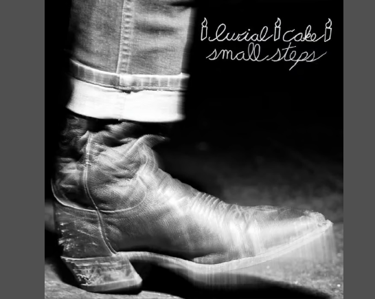 black and white image of a leg in rolled up denim pants and a beat up black cowboy boot tapping in motion. The words 'burial cake' small steps is in white lettering in the upper right corner of the image
