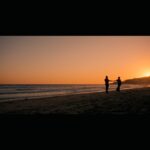 On a beach at sunset's orange hue, two people embrace