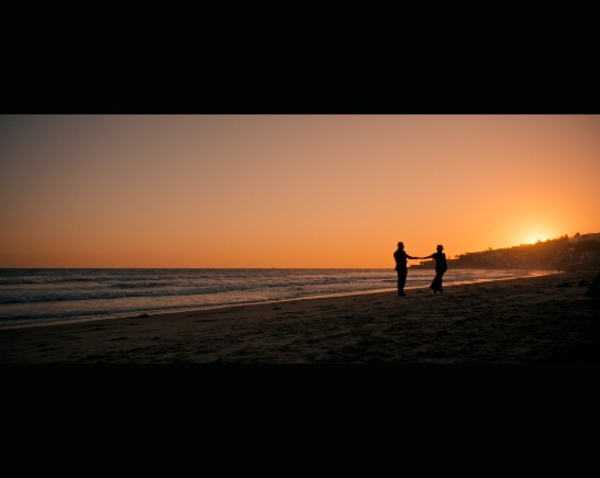 On a beach at sunset's orange hue, two people embrace