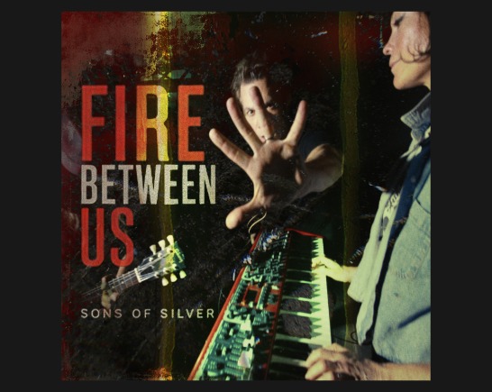 Music single cover for Sons of Silver song Fire Between Us in reds and deep browns. The keyboard player faces the left and the guitar player holds out his hand at the center of the image as if to stop us