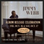 Songwriter Jimmy Webb sits at a grand piano in front of a window with sunlight streaming in.
